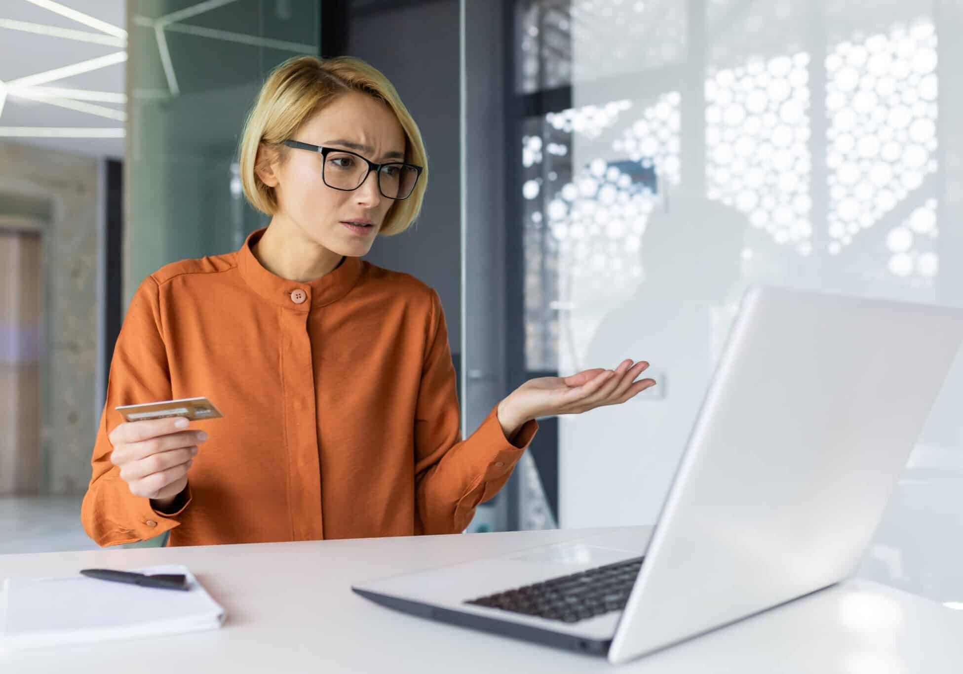 Sad And Unhappy Woman Inside Workplace Office With Laptop Holding Bank Credit Card Businesswoman Cheated Got Negative Account Balance And Online Money Transfer Error