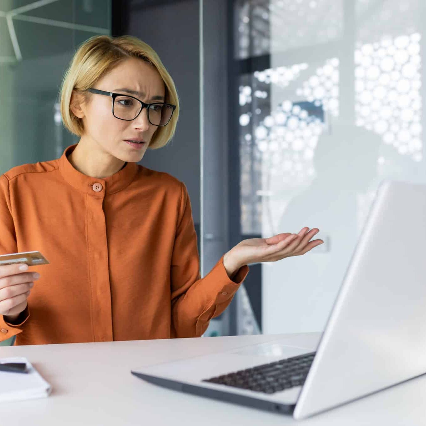 Sad And Unhappy Woman Inside Workplace Office With Laptop Holding Bank Credit Card Businesswoman Cheated Got Negative Account Balance And Online Money Transfer Error