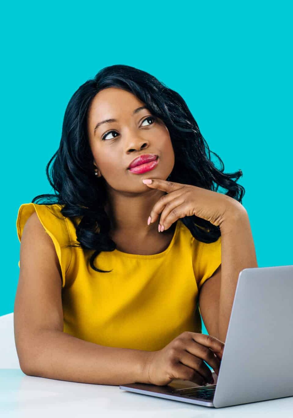 portrait of a young woman sitting behind desk and computer laptop, looking up thinking