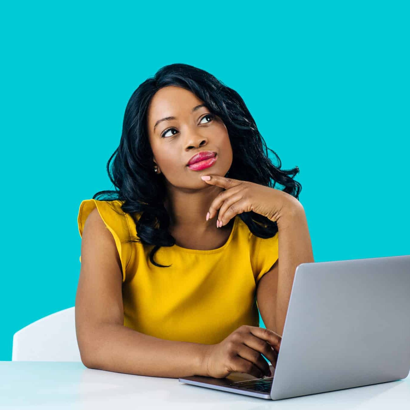 portrait of a young woman sitting behind desk and computer laptop, looking up thinking